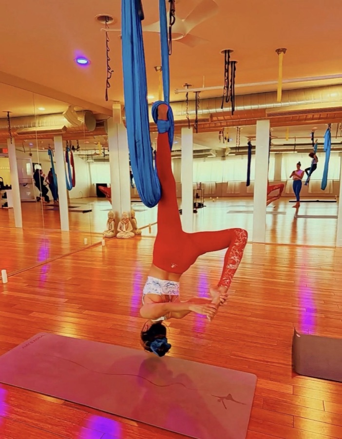 A student upside down in a red aerial silk.