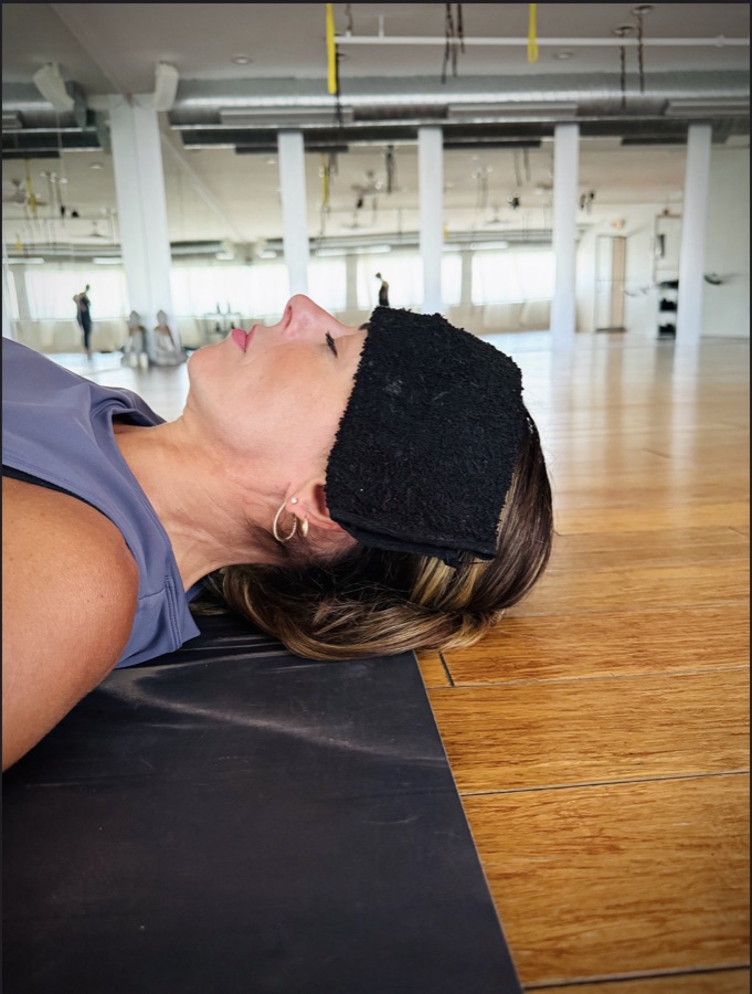 A student resting in savasana with a cool towel.