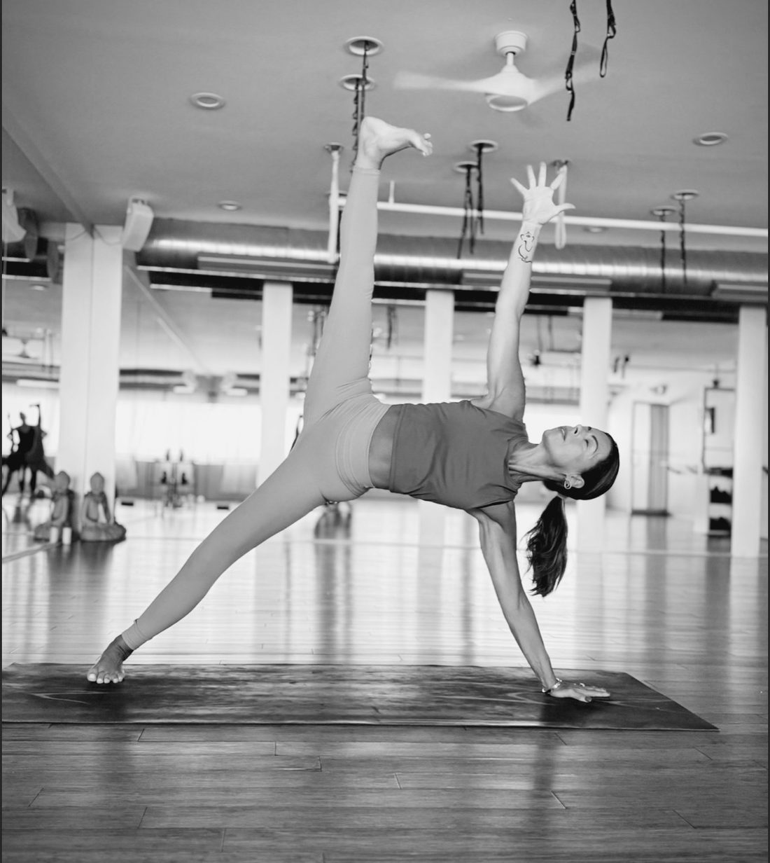 A teacher in side plank with her top arm reaching up, in the studio's long room.