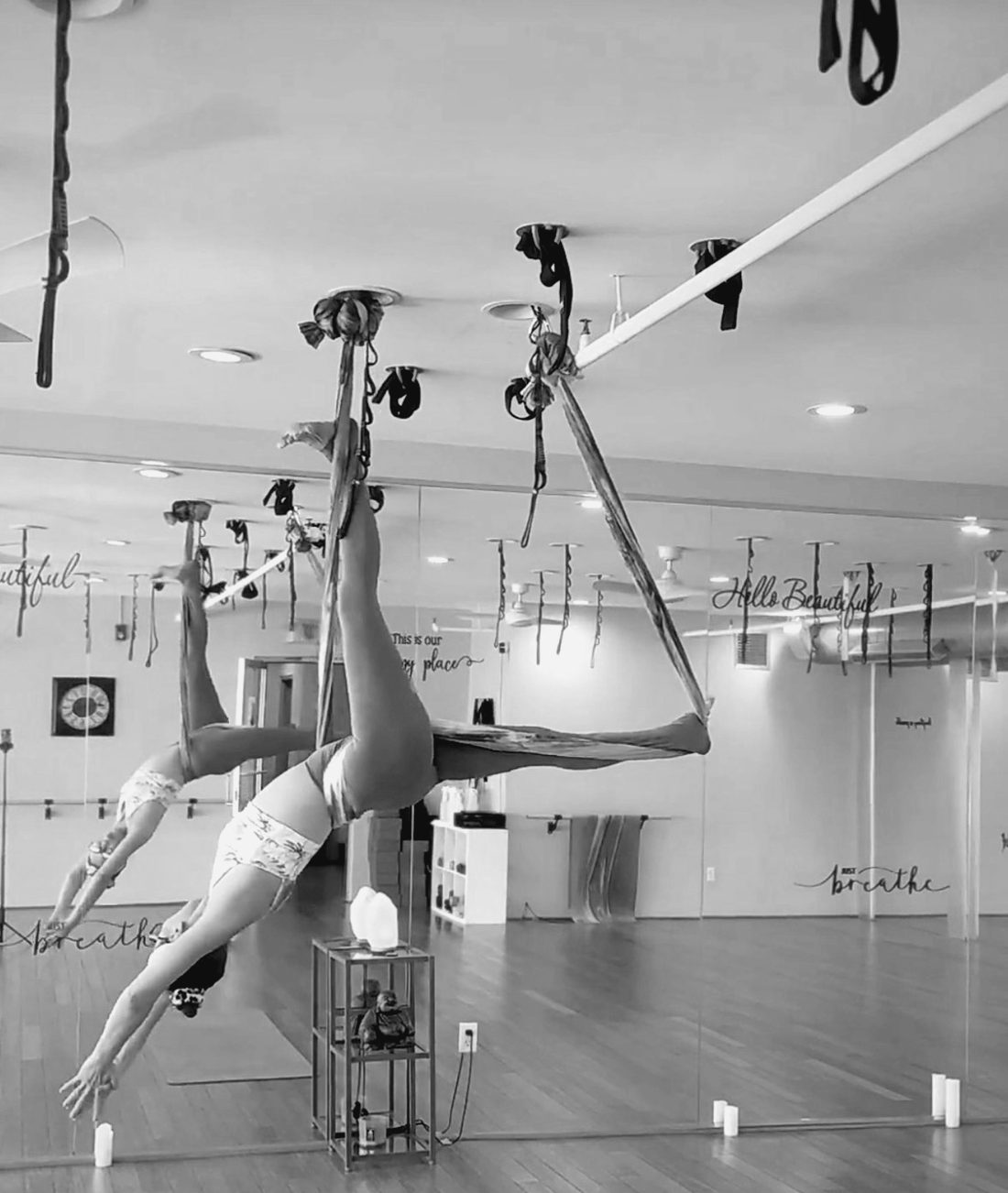 A student upside down in the silks, candles along the mirror.